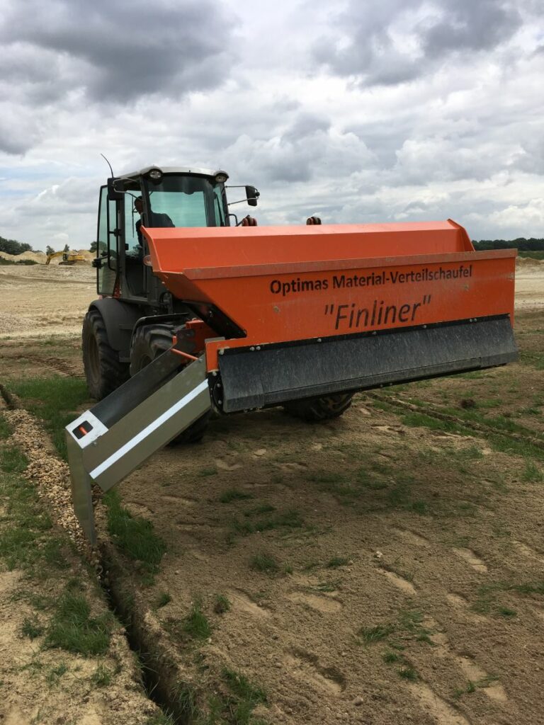 Gelungener Drainageeinsatz für Parookaville >Optimas Finliner-Materialverteileschaufel montiert an einem Radlader